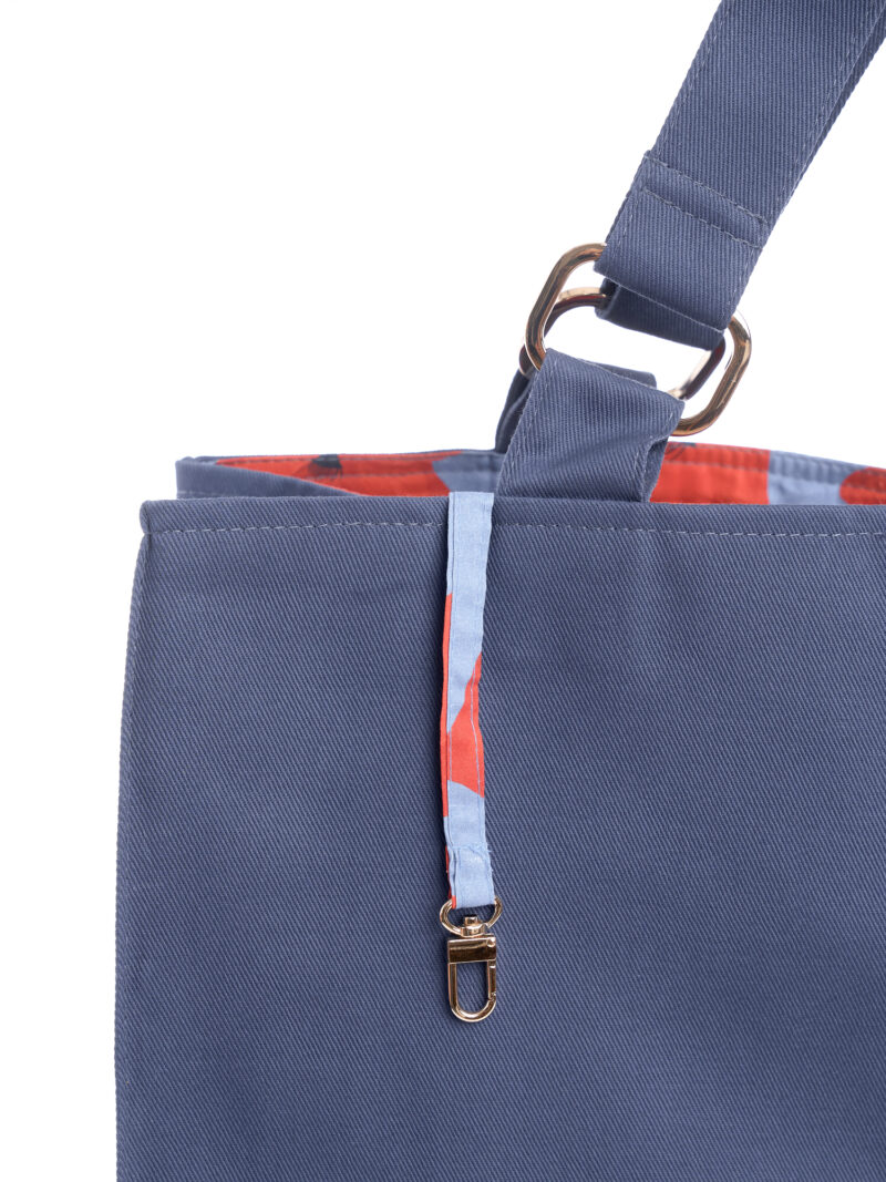 Torba shopperka Blue Meadow kolor granatowy jeans, niebieska podszewka w czerwone maki. Pokazany detal - karabińczyk do podpięcia kluczy lub kosmetyczki.